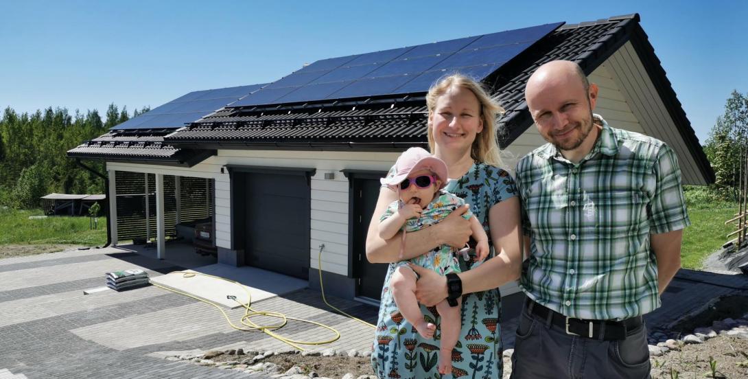 Two adults with a baby in front of a detached house. There are solar panels on the house's roof.