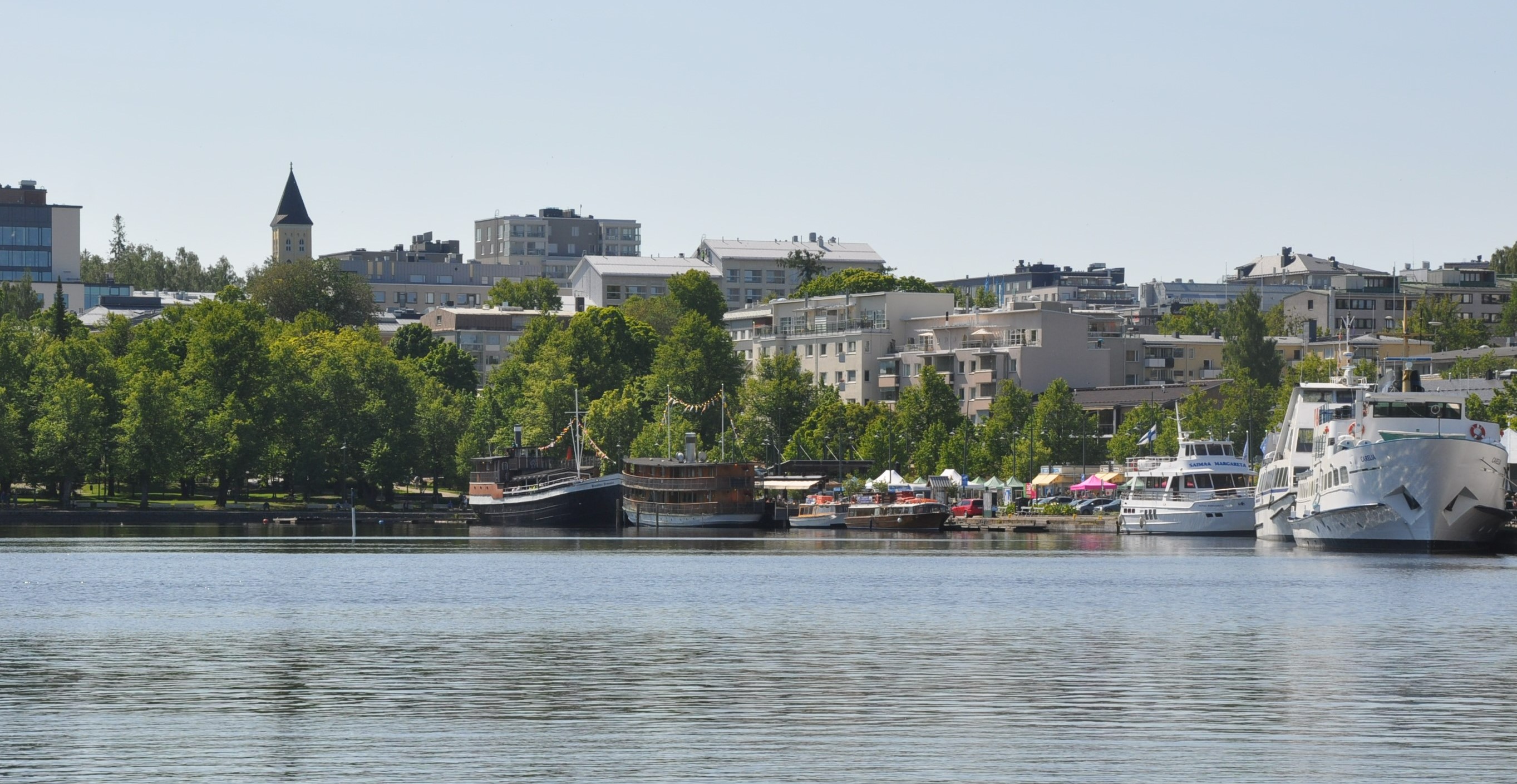 The harbor of Lappeenranta. In the front, boats. Green trees and city buildings in the background.