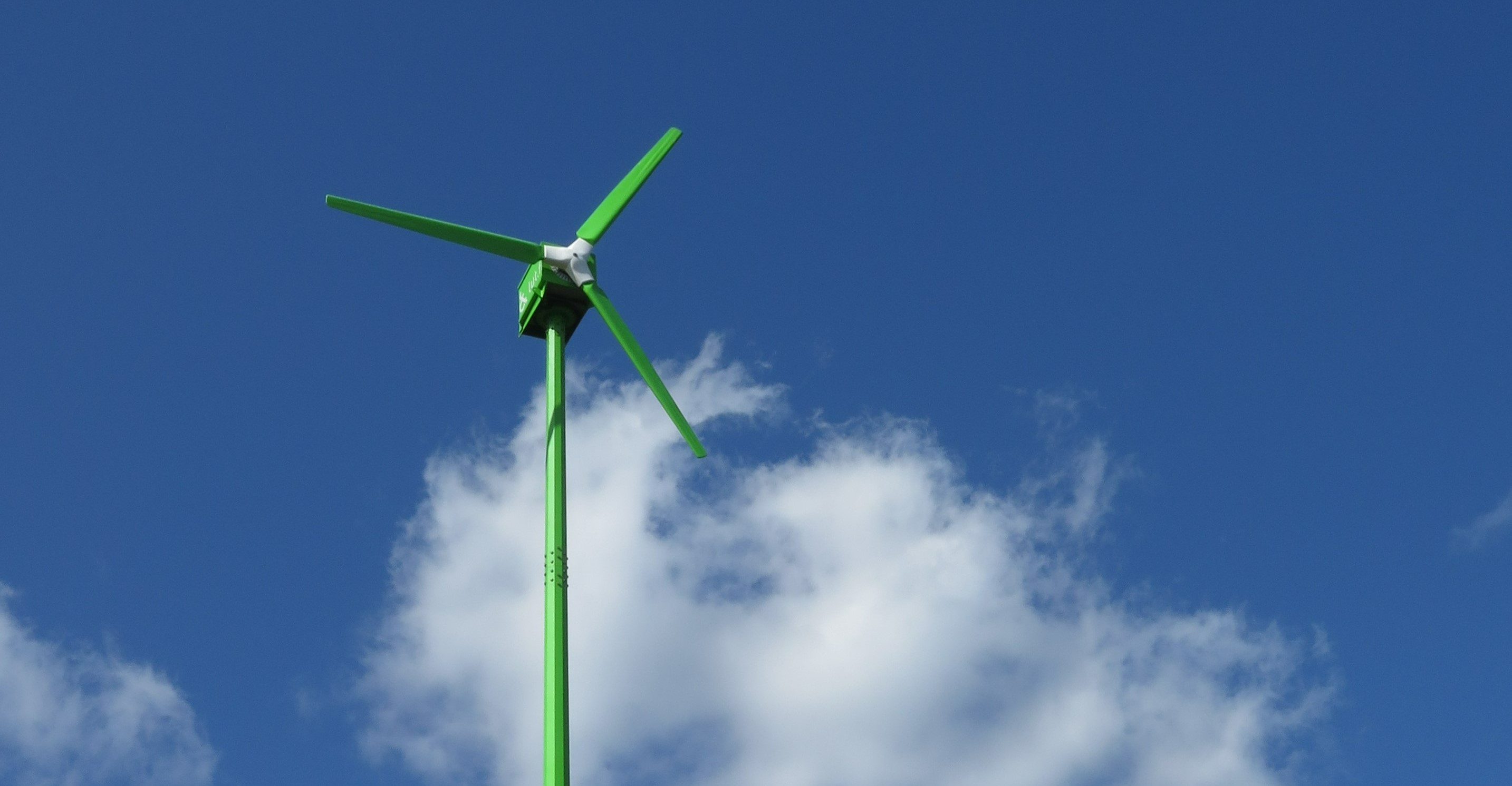 A green wind turbine. In the background, a blue sky.