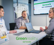 Kaksi miestä ja nainen istuvat neuvottelupöydän ääressä. Taustalla Greenreality Networkin markkinointimateriaaleja. Alareunassa vihreä Greenreality Network -logo.