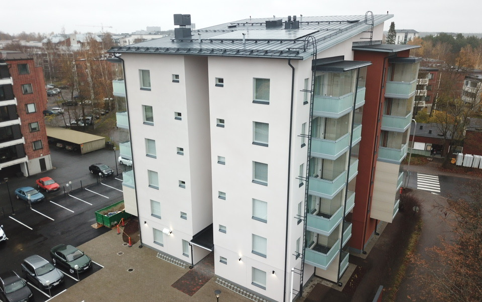 A light new apartment building with solar panels on the roof. Cars in the yard.